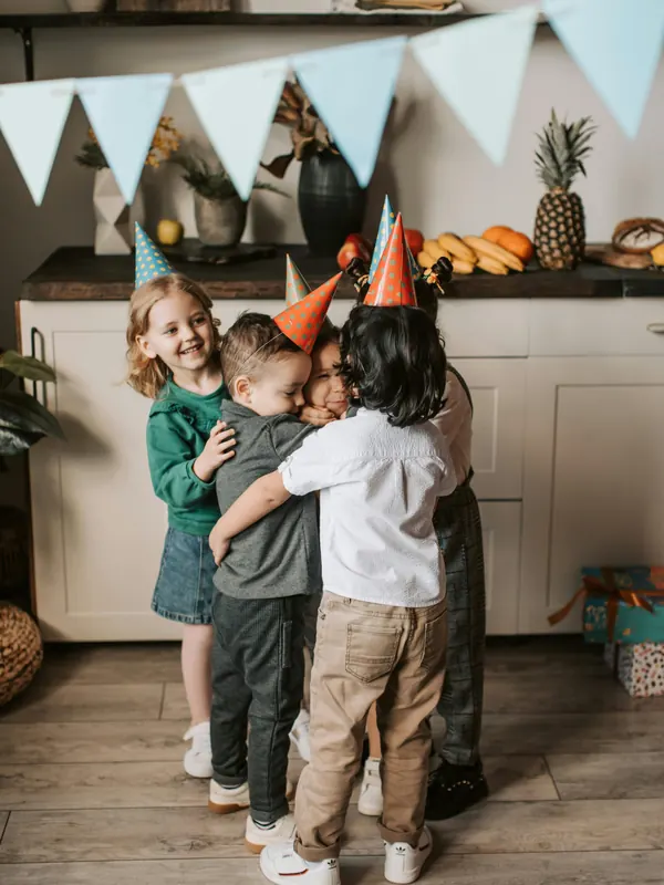 Kinder mit Partyhüten umarmen sich bei einer Geburtstagsfeier